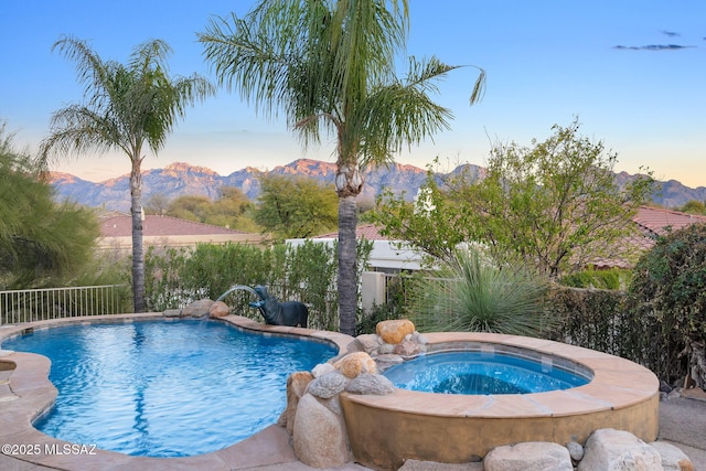 pool at dusk featuring a fenced in pool, an in ground hot tub, a fenced backyard, and a mountain view