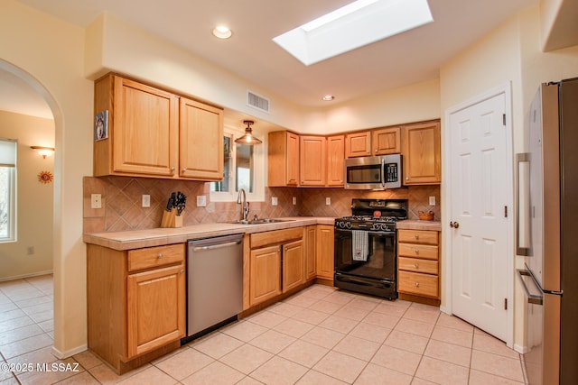 kitchen featuring sink, tasteful backsplash, a skylight, light tile patterned floors, and appliances with stainless steel finishes