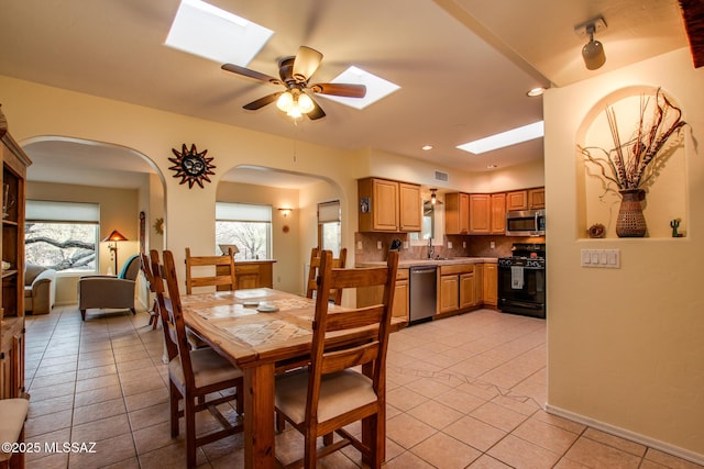 tiled dining area featuring ceiling fan, a skylight, and sink