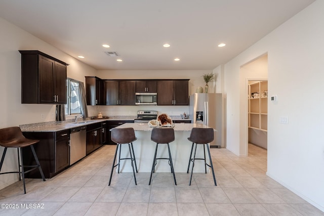 kitchen featuring dark brown cabinets, appliances with stainless steel finishes, sink, a kitchen bar, and a kitchen island