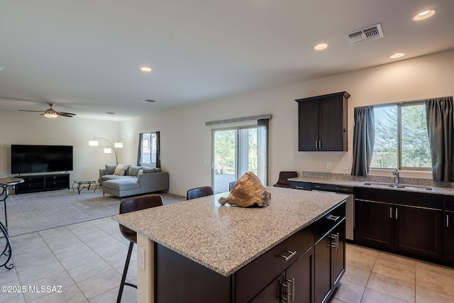 kitchen with dishwasher, sink, light tile patterned floors, a kitchen island, and dark brown cabinetry