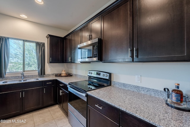 kitchen with dark brown cabinetry, appliances with stainless steel finishes, sink, light tile patterned flooring, and light stone counters