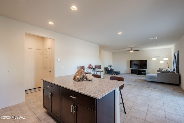 kitchen featuring light stone countertops, a center island, a kitchen bar, ceiling fan, and dark brown cabinets