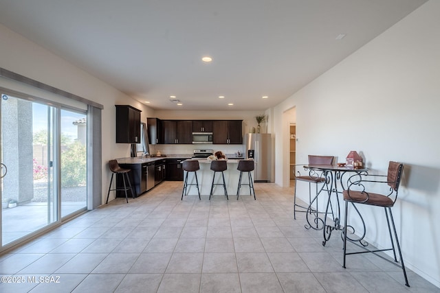 kitchen featuring appliances with stainless steel finishes, a kitchen island, a breakfast bar, light tile patterned floors, and dark brown cabinets