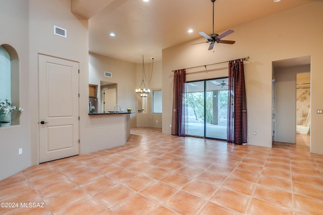 unfurnished living room with light tile patterned floors, sink, ceiling fan with notable chandelier, and a high ceiling