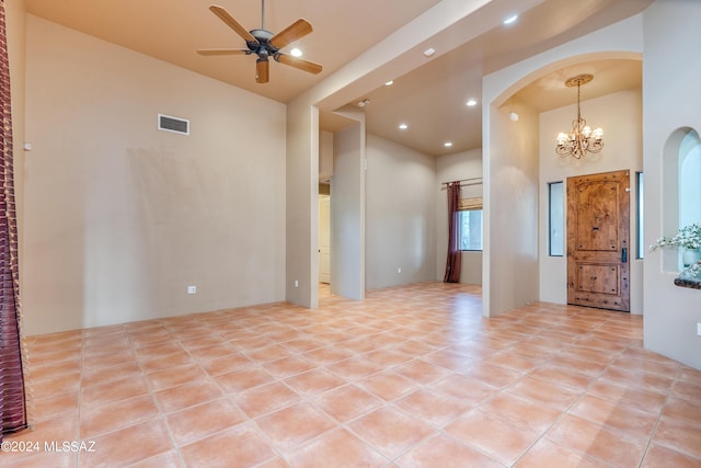 empty room with a towering ceiling, ceiling fan with notable chandelier, and light tile patterned flooring