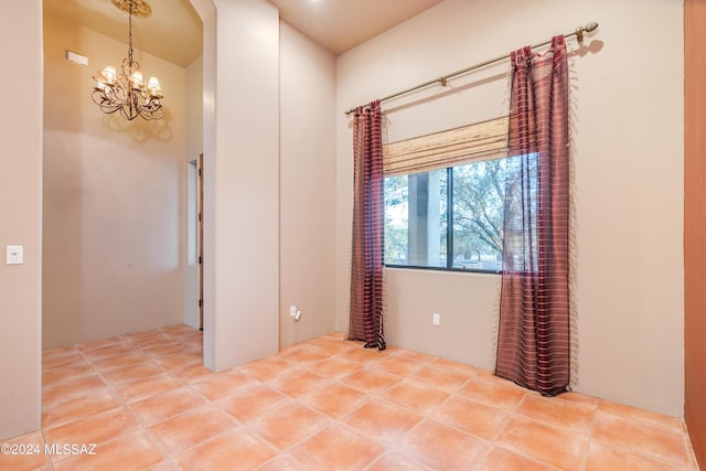 tiled spare room featuring an inviting chandelier