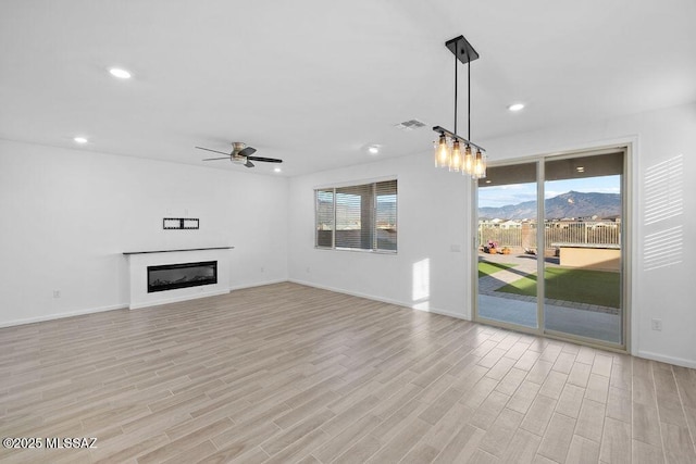 unfurnished living room featuring a mountain view, ceiling fan, and light wood-type flooring