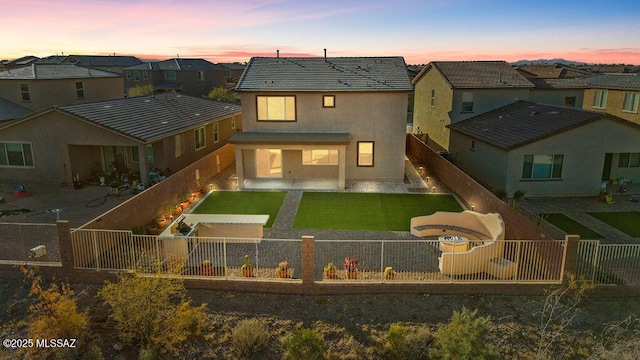 back house at dusk featuring a patio and a lawn