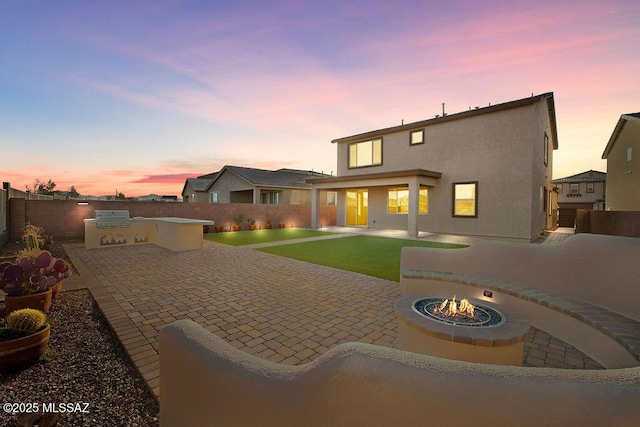 back house at dusk with a patio, an outdoor kitchen, and a fire pit