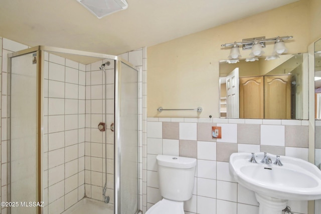 bathroom featuring toilet, sink, tile walls, and a shower with shower door