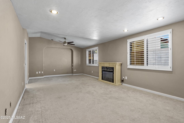 unfurnished living room with baseboards, arched walkways, ceiling fan, carpet flooring, and a fireplace