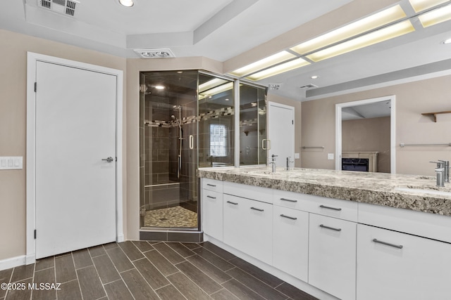 full bathroom featuring wood finish floors, a sink, visible vents, double vanity, and a stall shower