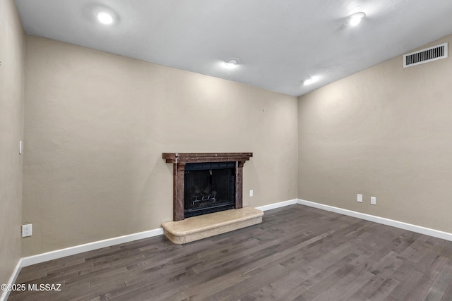 unfurnished living room with visible vents, a fireplace with raised hearth, vaulted ceiling, wood finished floors, and baseboards