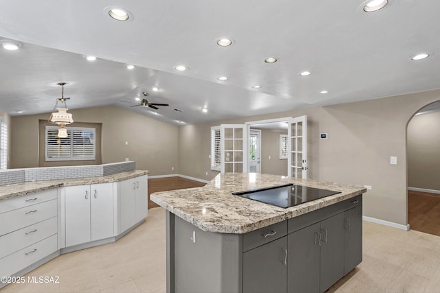 kitchen with lofted ceiling, arched walkways, black electric cooktop, white cabinetry, and a center island