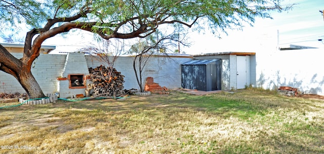 back of house with exterior fireplace, a lawn, and a storage unit