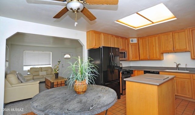 kitchen with sink, black fridge, a kitchen island, ceiling fan, and gas range oven