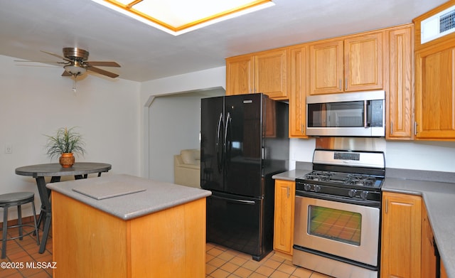 kitchen with a kitchen island, appliances with stainless steel finishes, a breakfast bar area, light tile patterned floors, and ceiling fan