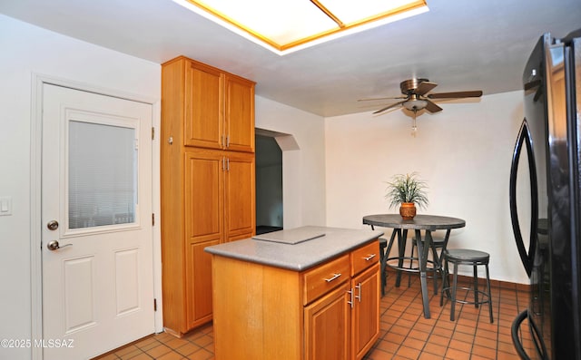 kitchen with a center island, black refrigerator, light tile patterned floors, and ceiling fan