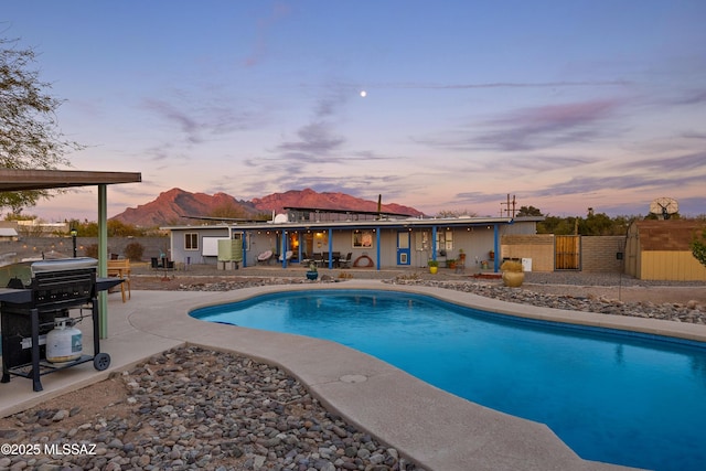 pool at dusk with a mountain view, area for grilling, and a patio area