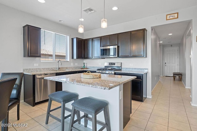 kitchen featuring hanging light fixtures, dark brown cabinets, stainless steel appliances, light stone countertops, and a kitchen island