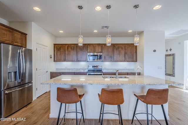 kitchen with an island with sink, appliances with stainless steel finishes, light hardwood / wood-style floors, and sink