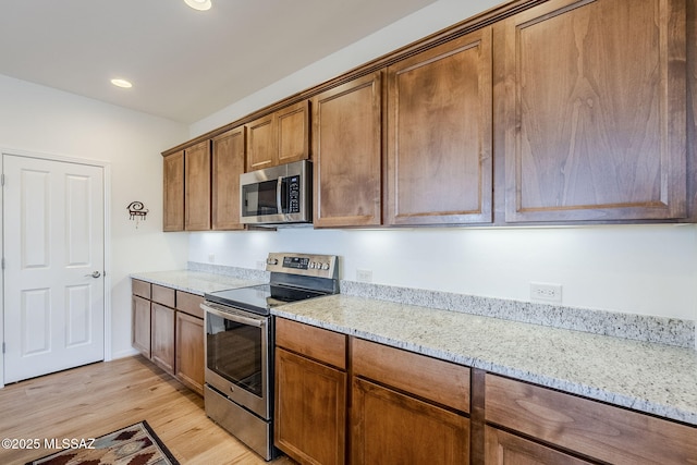 kitchen featuring light wood-type flooring, light stone countertops, and appliances with stainless steel finishes