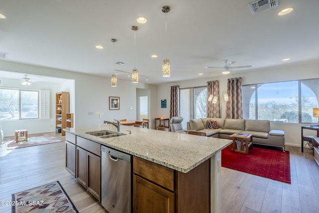 kitchen featuring a kitchen island with sink, sink, stainless steel dishwasher, and light stone countertops