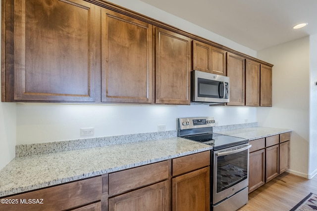 kitchen with light stone countertops, stainless steel appliances, and light wood-type flooring