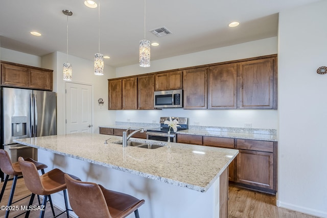 kitchen featuring pendant lighting, an island with sink, a kitchen bar, light hardwood / wood-style floors, and stainless steel appliances