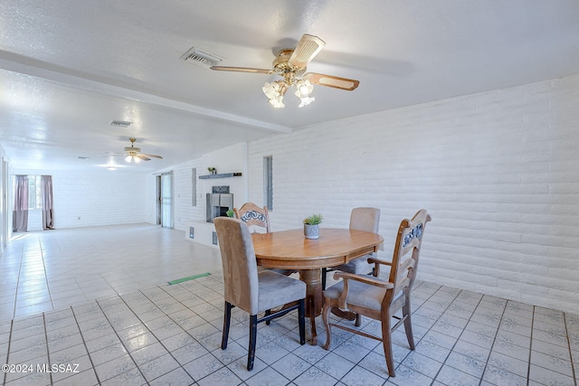 dining room featuring a textured ceiling, beam ceiling, brick wall, visible vents, and a ceiling fan