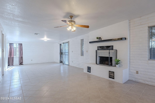 unfurnished living room featuring lofted ceiling, light tile patterned floors, a fireplace with raised hearth, brick wall, and a ceiling fan