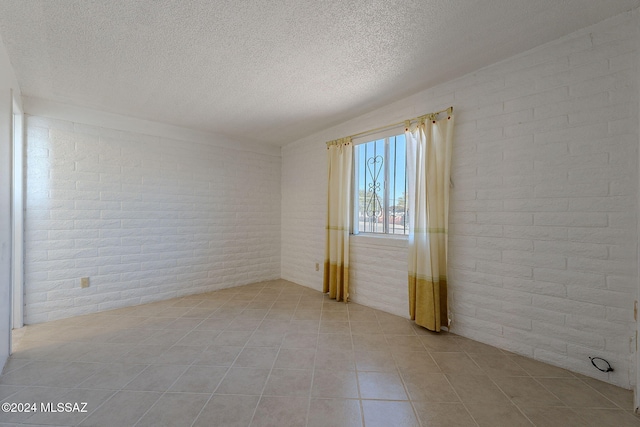 empty room with light tile patterned floors, brick wall, and a textured ceiling