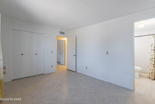 unfurnished bedroom with a closet, a textured ceiling, visible vents, ensuite bath, and light tile patterned floors