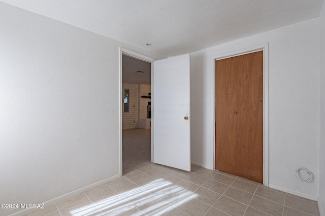 empty room featuring light tile patterned flooring, baseboards, and a textured ceiling