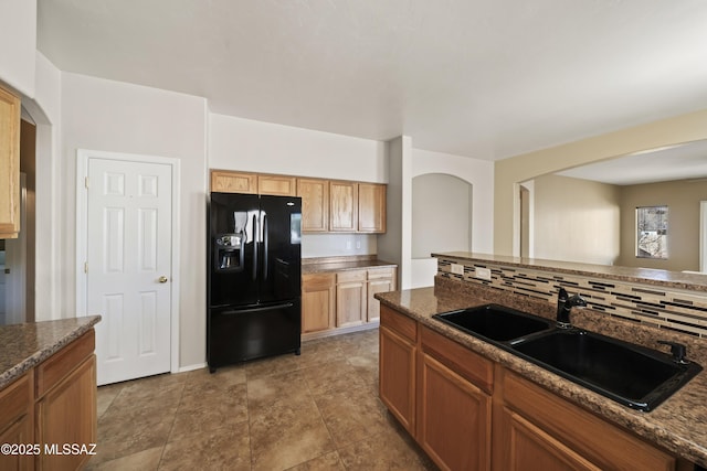 kitchen featuring black fridge with ice dispenser, sink, decorative backsplash, and dark stone countertops