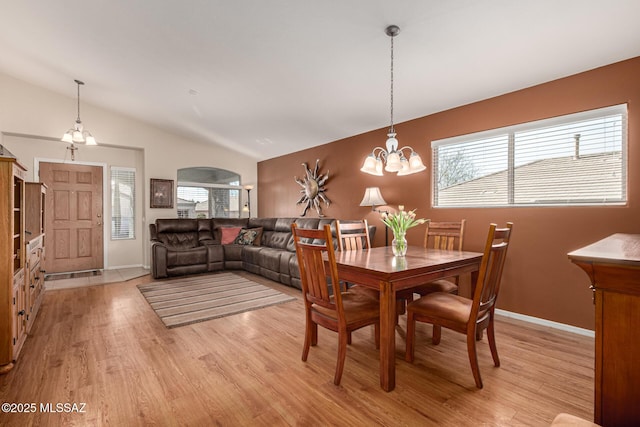 dining space with vaulted ceiling, baseboards, light wood-style flooring, and an inviting chandelier