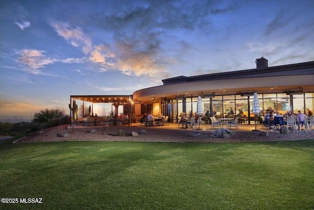 back house at dusk featuring a lawn