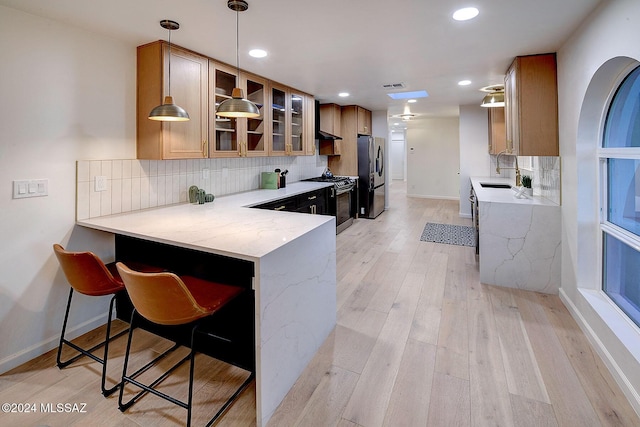 kitchen with appliances with stainless steel finishes, decorative backsplash, light hardwood / wood-style floors, kitchen peninsula, and a breakfast bar