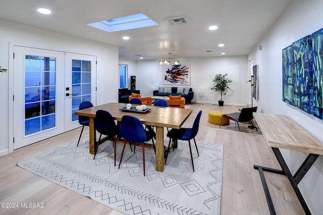 dining area featuring a chandelier, light hardwood / wood-style flooring, a skylight, and french doors