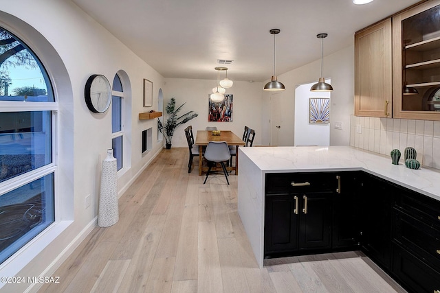 kitchen featuring light stone countertops, decorative light fixtures, decorative backsplash, kitchen peninsula, and light wood-type flooring