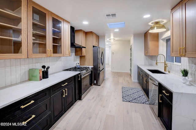 kitchen featuring sink, wall chimney range hood, light hardwood / wood-style flooring, stainless steel appliances, and light stone counters