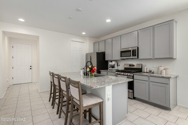 kitchen featuring stainless steel appliances, light stone countertops, gray cabinets, and a center island with sink