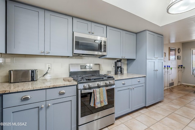 kitchen featuring light tile patterned floors, backsplash, appliances with stainless steel finishes, and gray cabinetry