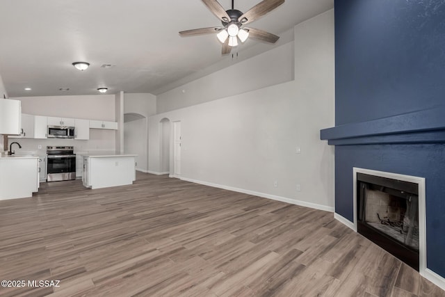 unfurnished living room with vaulted ceiling, ceiling fan, sink, light wood-type flooring, and a large fireplace