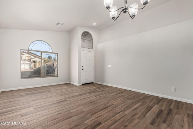 empty room featuring wood-type flooring, vaulted ceiling, and a notable chandelier