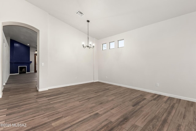 unfurnished room featuring vaulted ceiling, an inviting chandelier, dark hardwood / wood-style floors, and a fireplace