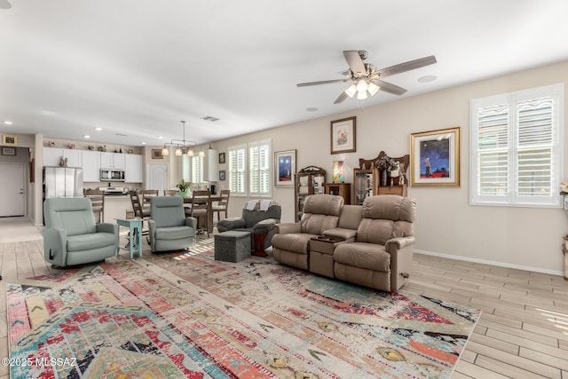 living area with baseboards, light wood-type flooring, ceiling fan with notable chandelier, and recessed lighting