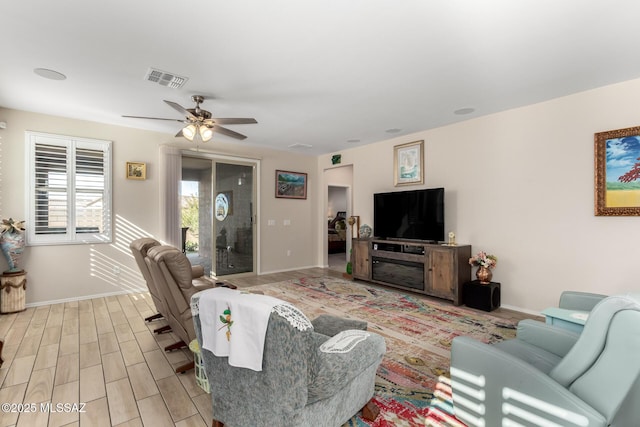 living room featuring baseboards, visible vents, light wood-type flooring, and a ceiling fan