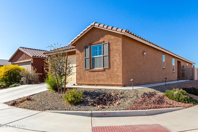 view of home's exterior with a garage, stucco siding, driveway, and a tiled roof